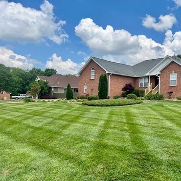 A brick house with a neatly mowed lawn under a blue sky with clouds.