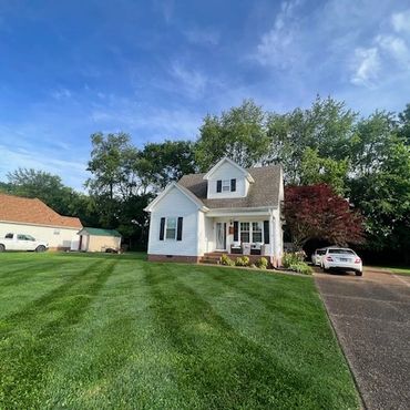 A charming white house with a well-maintained lawn and driveway under a blue sky.