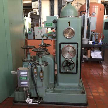 Vintage industrial machine with pressure gauges and control valves in a factory setting.