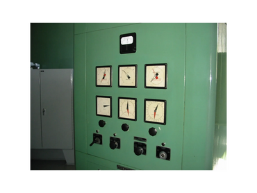 Green industrial control panel with gauges and knobs in a utility room.