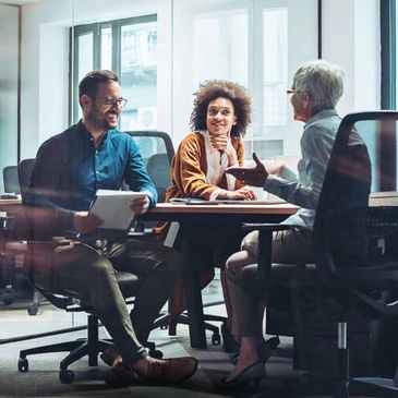 Three professionals engaged in a lively office discussion around a table.