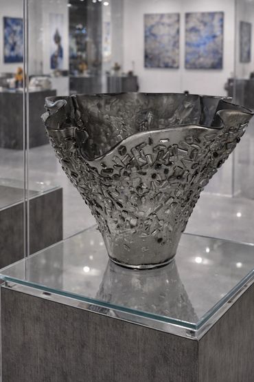 Intricate textured glass vase displayed on a pedestal in an art gallery.