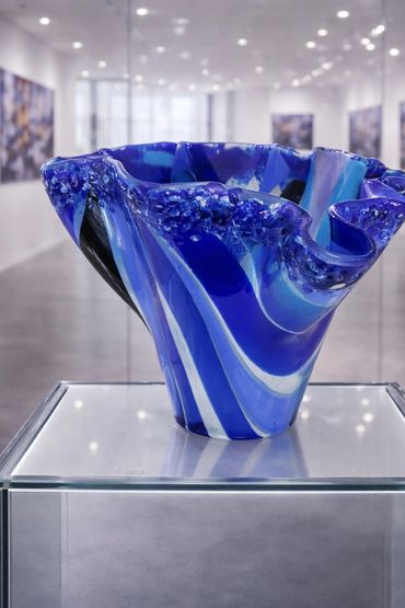 Blue glass art piece with swirling patterns displayed in a gallery.