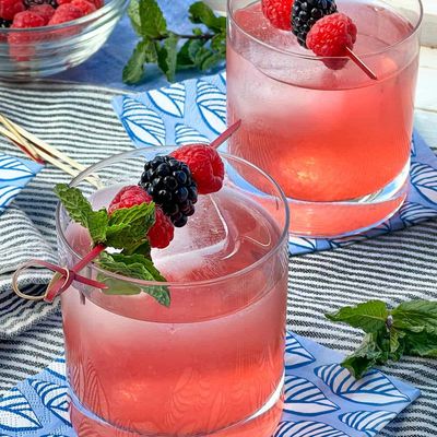 Two refreshing pink berry cocktails garnished with fresh berries and mint.