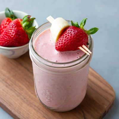 Strawberry smoothie garnished with a fresh strawberry and banana slice on a wooden board.
