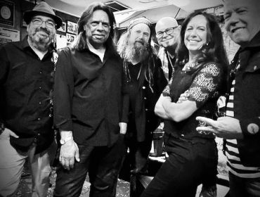 Group of six people posing happily indoors in black and white.