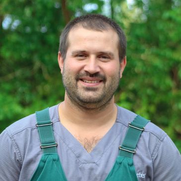 Smiling man wearing green overalls outdoors.