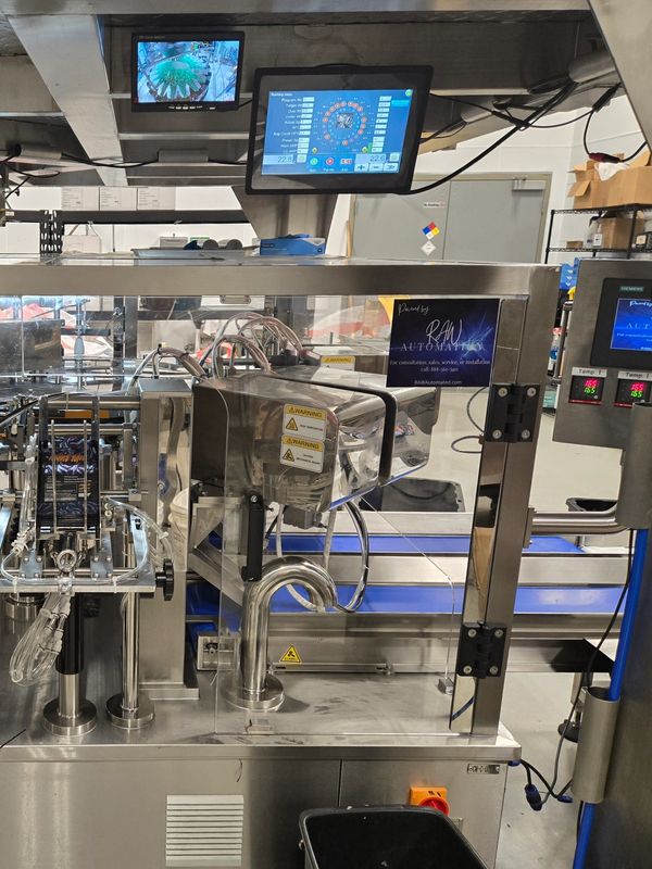 Industrial packaging machine with control monitors and safety warnings in a factory setting.
