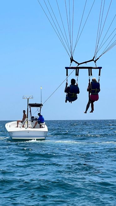 Two people parasailing behind a boat on a sunny day.