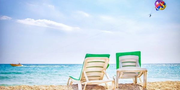 Two empty beach chairs face the sea with a parasailer in the sky.