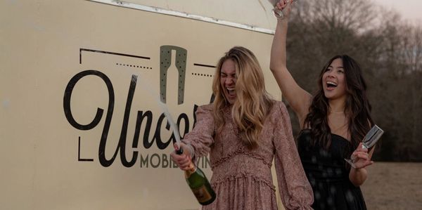 Two women celebrating with champagne outdoors near a mobile bar.