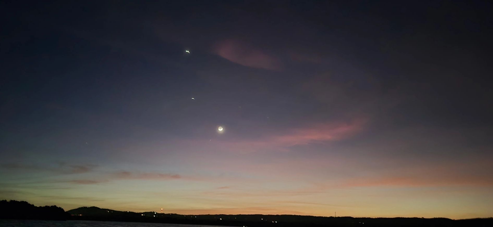 Twilight sky with crescent moon and horizon silhouette.