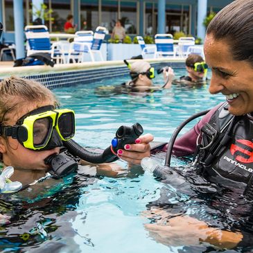 Instructor teaching child scuba diving in pool.