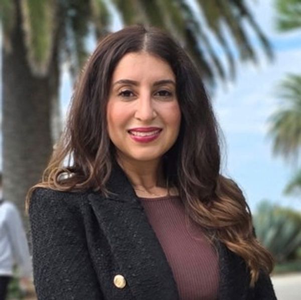 Woman smiling outdoors with palm trees in background.
