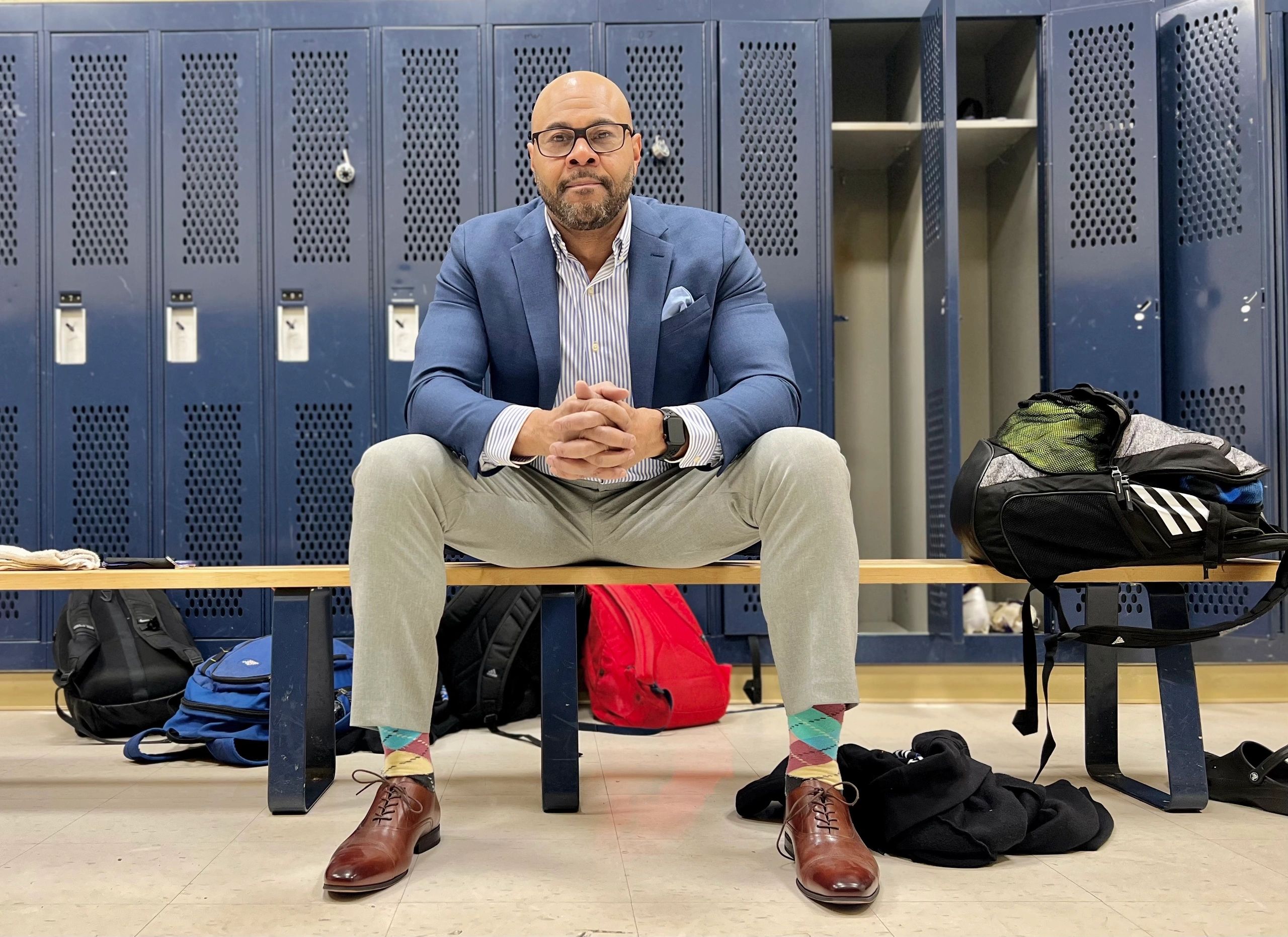 Man in a suit sitting on a bench in a locker room.