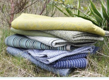 A stack of folded, colourful fabric is placed outside on the grass surrounded by foliage. 