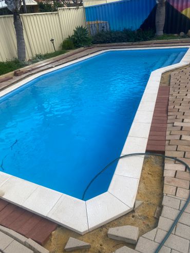 A backyard pool with clear blue water and partially unfinished brick paving.