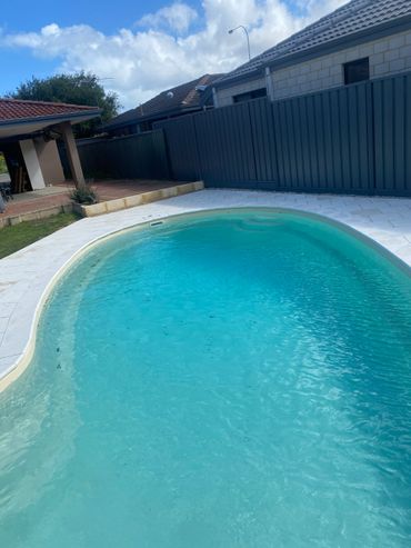 A clear backyard swimming pool with blue water and surrounding patio.
