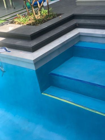 Empty blue swimming pool with steps and surrounding garden area.