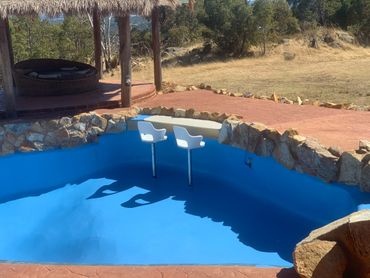 Empty blue pool with white bar stools and rustic stone and wood decor.