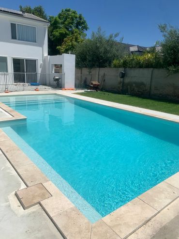 A clear blue swimming pool in a sunny backyard next to a white house.