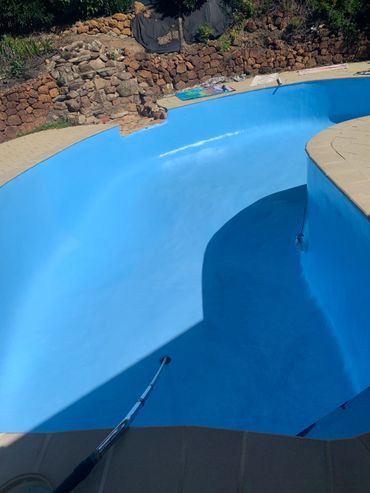 Empty blue swimming pool with stone wall and cleaning equipment.