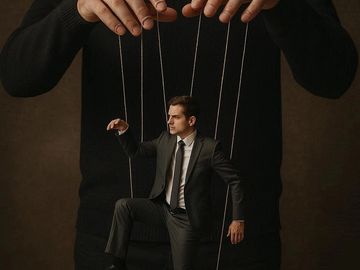 A man in a suit controlled like a marionette by strings.