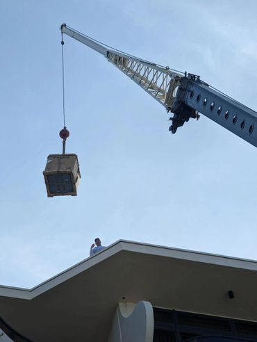 Crane lifting a large boxed item above a building with a person watching.