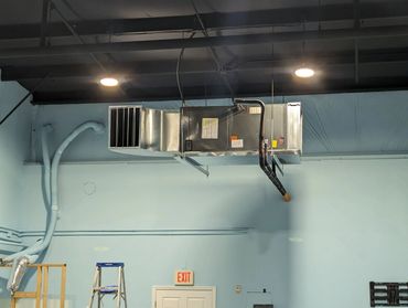 Industrial ventilation system mounted on ceiling with ladders below.