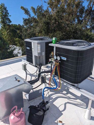 Two HVAC units on a rooftop with maintenance equipment and gauges attached.