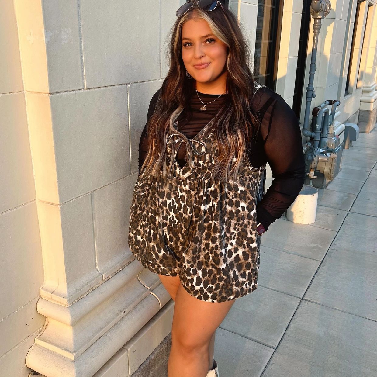 Woman in leopard print outfit stands confidently by a building in warm sunlight.