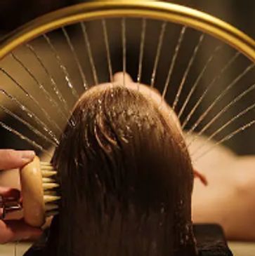 A person receiving a gentle hair wash with a wooden brush.