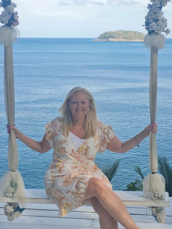 Woman in floral dress sitting on a decorated swing by the sea.