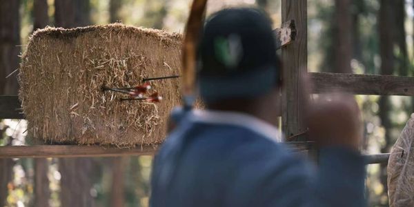 Archer aiming at a hay bale target with multiple arrows.
