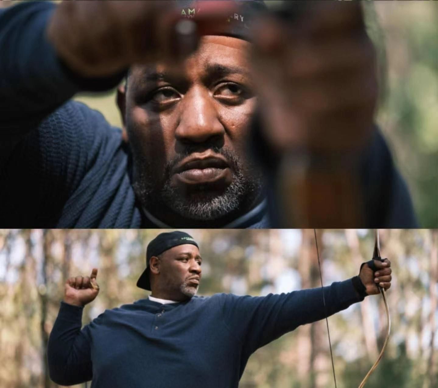 Man aiming a bow and arrow with intense focus in the woods.