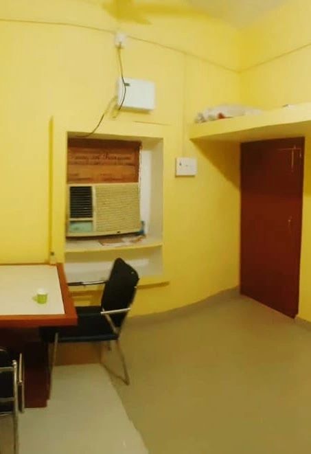 Simple yellow-painted room with a desk, chair, and window air conditioner.