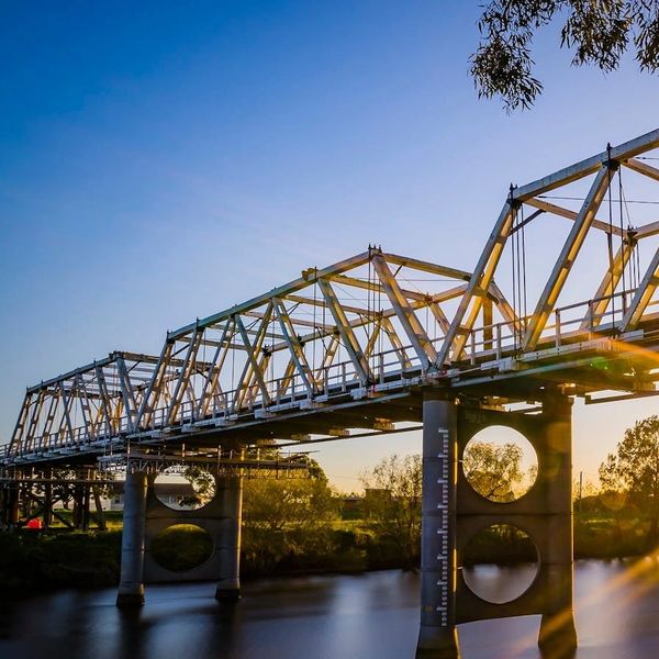 Sunset shining through a steel truss bridge over a river local to Property Management Company