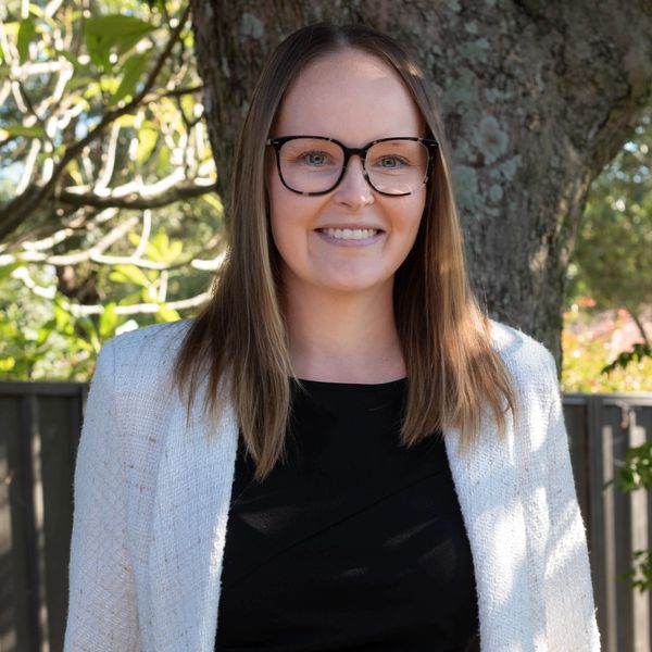 Smiling woman with glasses standing outdoors.