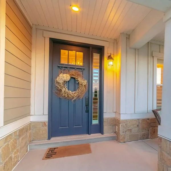 Cozy porch with a blue door, wreath, and seating area under warm lighting.