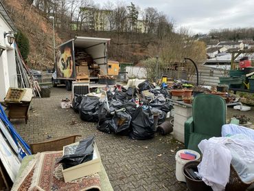 Transporter mit Hebebühne beim Beladen von Gerümpel im Hof während einer laufenden Hausentrümpelung