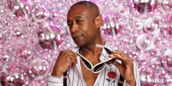 Man posing with sunglasses against a sparkling backdrop.