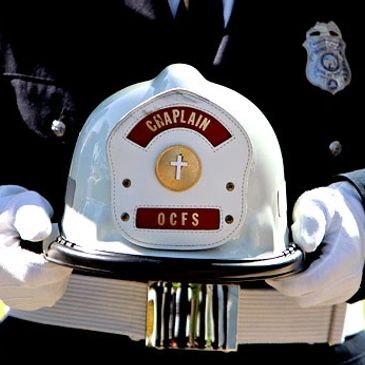 A firefighter's chaplain helmet held with white gloves.
