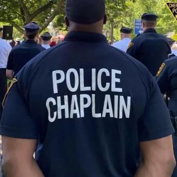 Police chaplain stands among officers outdoors.