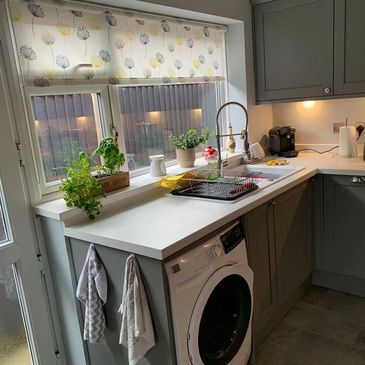 Modern kitchen with washing machine and plants near window.