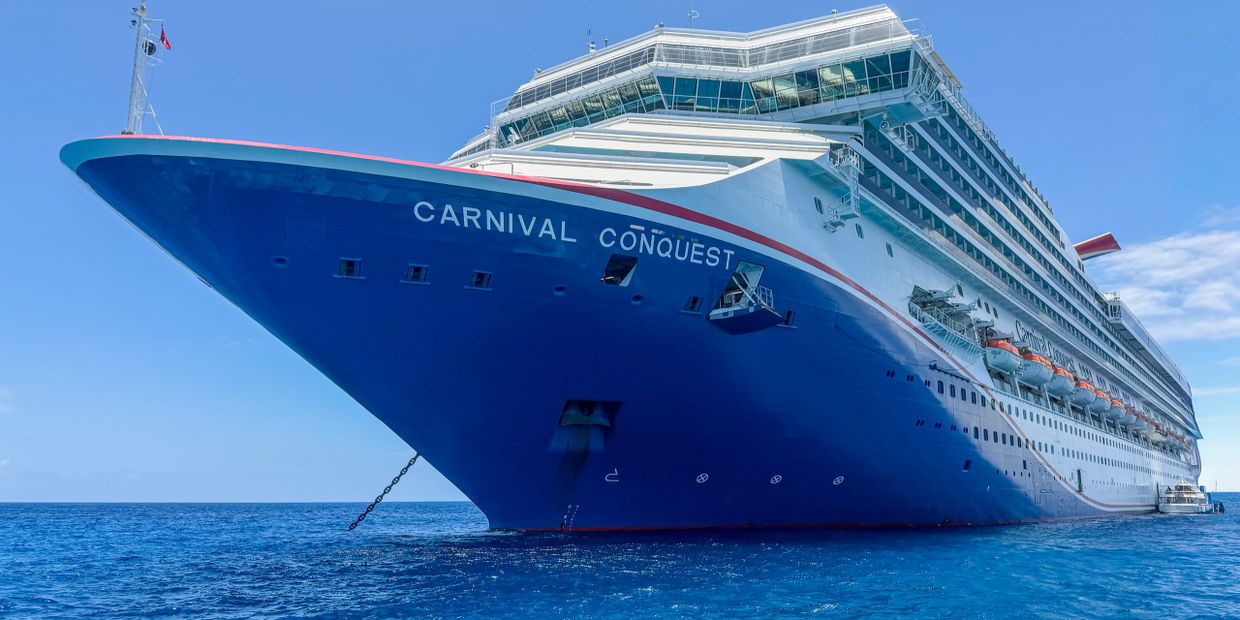 A large blue and white cruise ship named Carnival Conquest on the ocean.