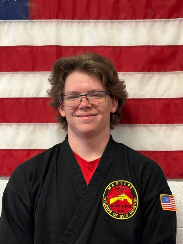 Young martial artist in black gi with American flag backdrop.
