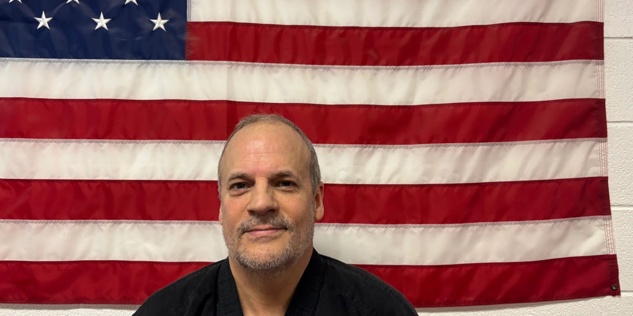 Man in black attire posing before an American flag.