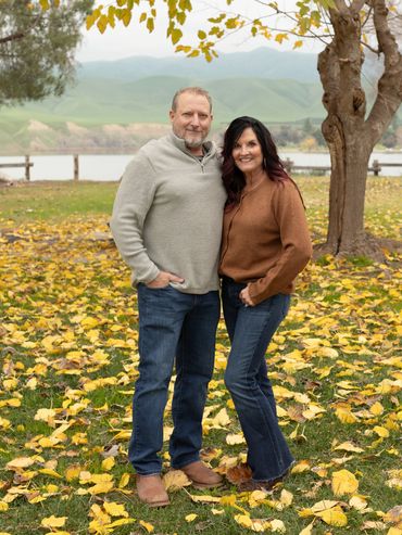 Couple standing outdoors in autumn with fallen leaves.