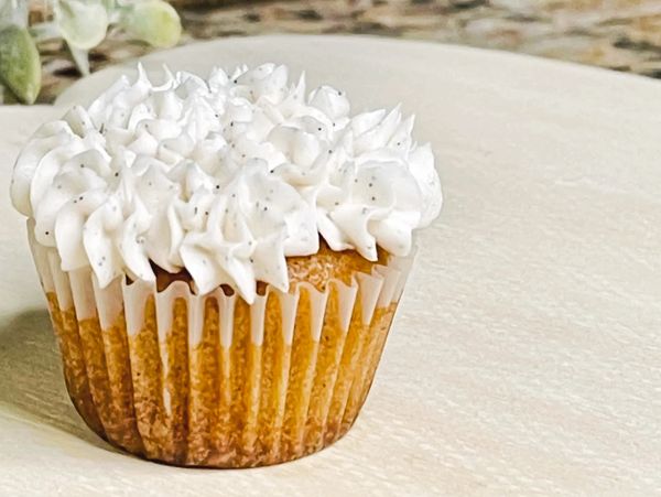 A frosted, vanilla bean mini-cupcake on a wooden serving plate