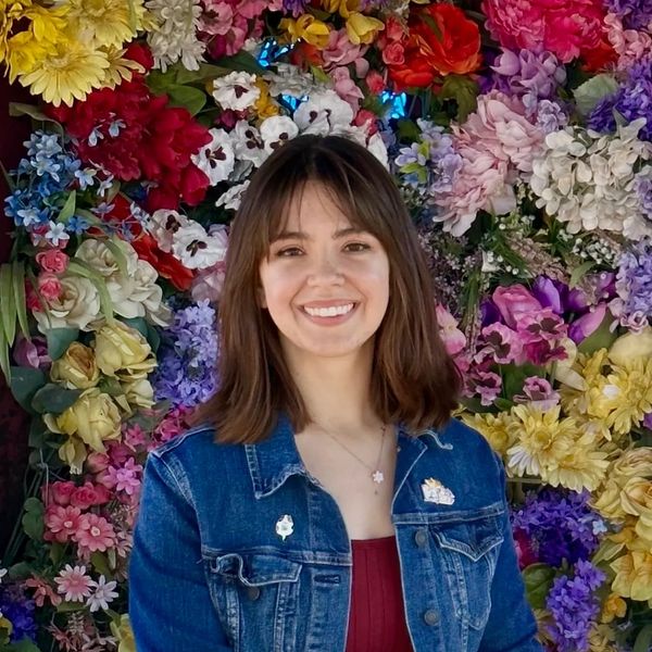 A smiling woman stands in front of a colorful flower wall.